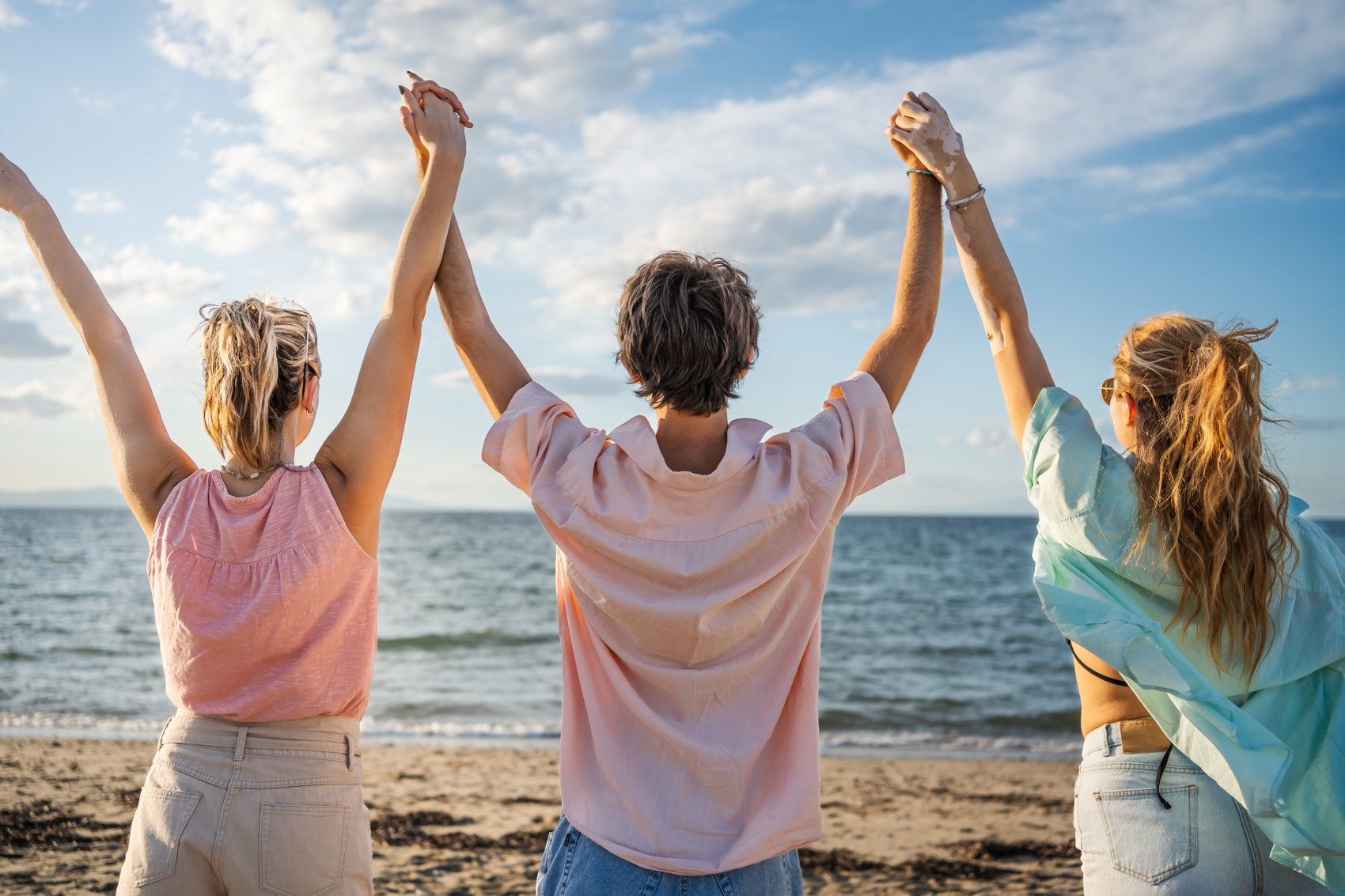 Friends together by the sea, hands raised in the light
